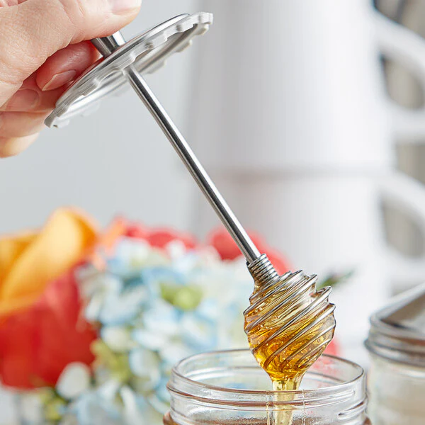 Cuillère à miel en inox alimentaire plongeant dans un pot de miel