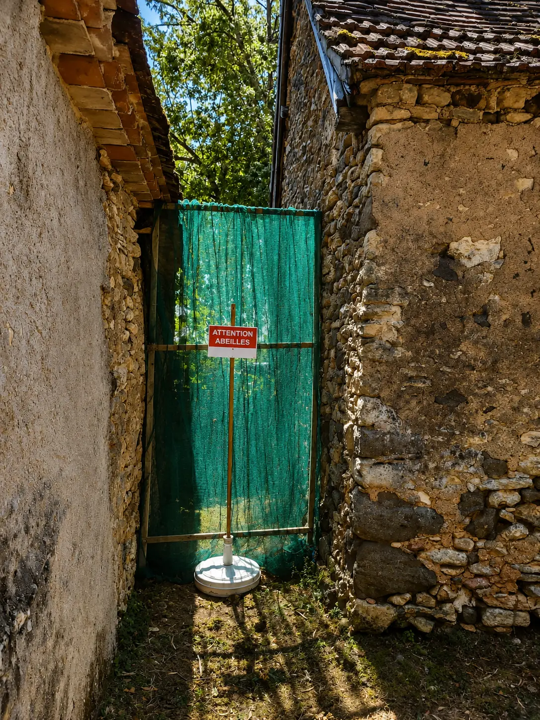 Cloison grillagée installée entre deux maisons en pierre afin de sécuriser le passage tout en préservant une colonie d'abeilles.
